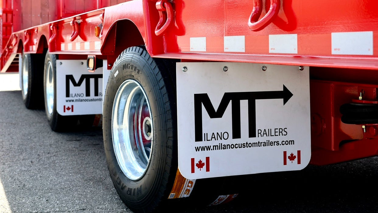 Red trailer with 'Milano Trailers' branding in front of a building.